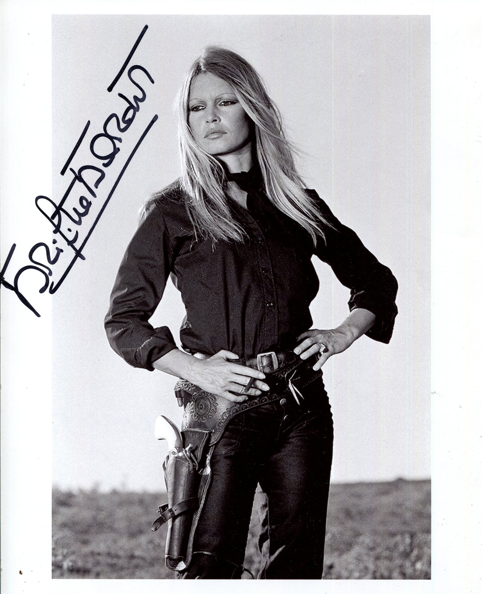 BARDOT BRIGITTE: (1934- ): BARDOT BRIGITTE: (1934- ) French Actress and sex symbol. Signed 8 x 10 photograph, the image showing Bardot standing in a three-quarter length pose, with a cigarette in hand and a revolver to her belt
