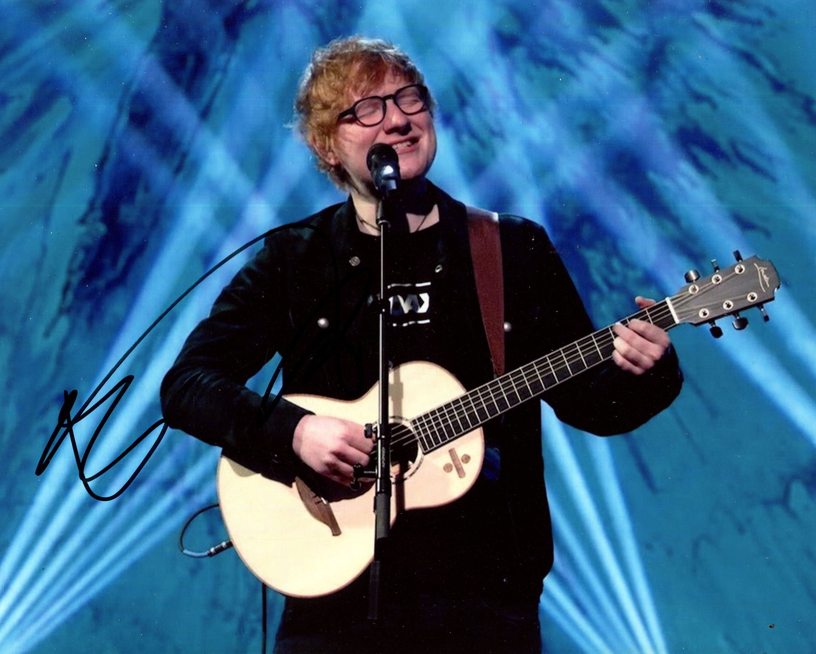 SHEERAN ED: (1991- ): SHEERAN ED: (1991- ) English singer & songwriter. Signed colour 10 x 8 photograph of Sheeran standing in a half-length pose as he performs with his guitar before a microphone. Signed in black ink