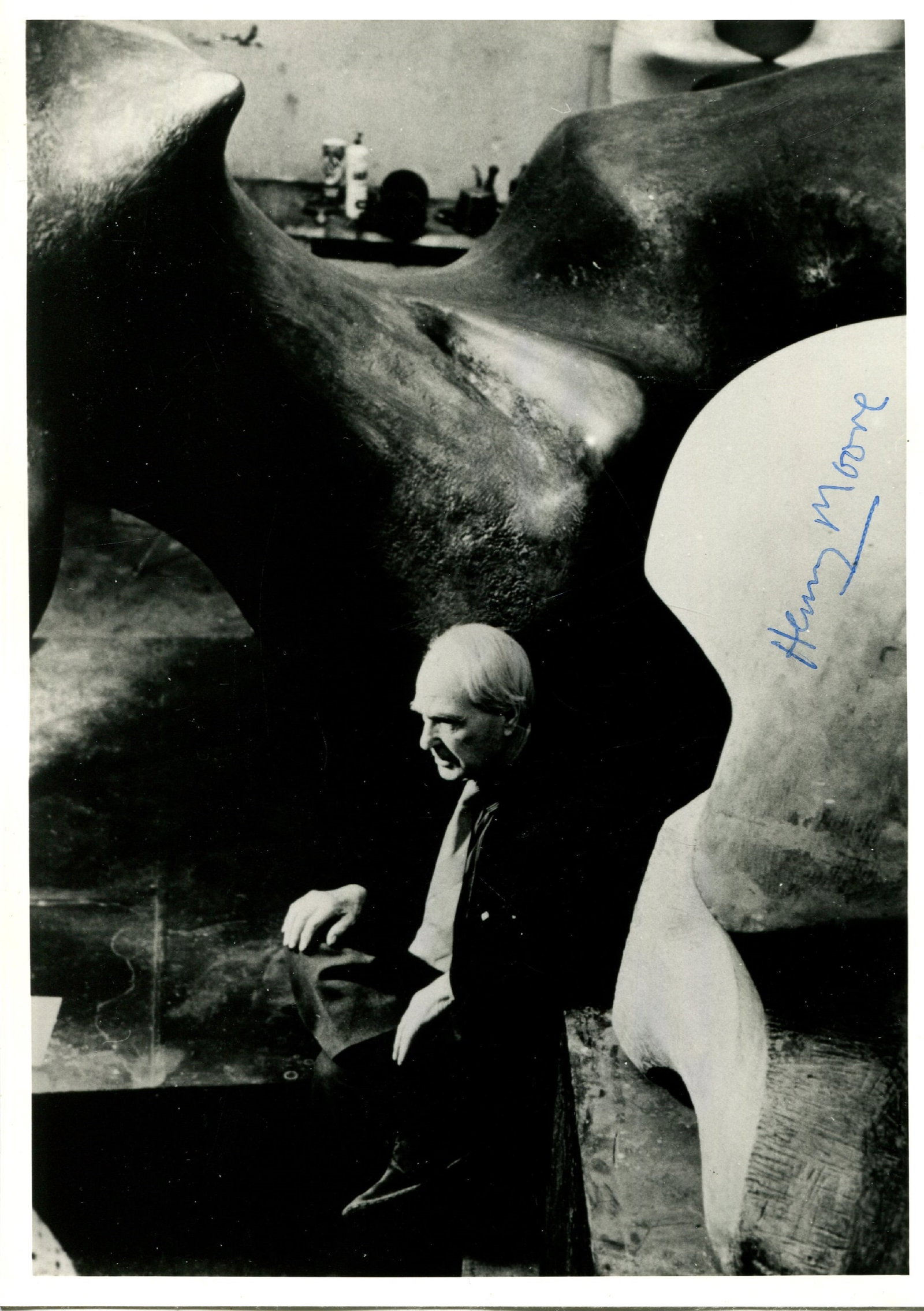 MOORE HENRY: (1898-1986): MOORE HENRY: (1898-1986) English sculptor and artist. Signed 5 x 7 photograph of Moore seated in a full-length pose within his studio, engulfed by two large sculptures. Signed in blue ink with his