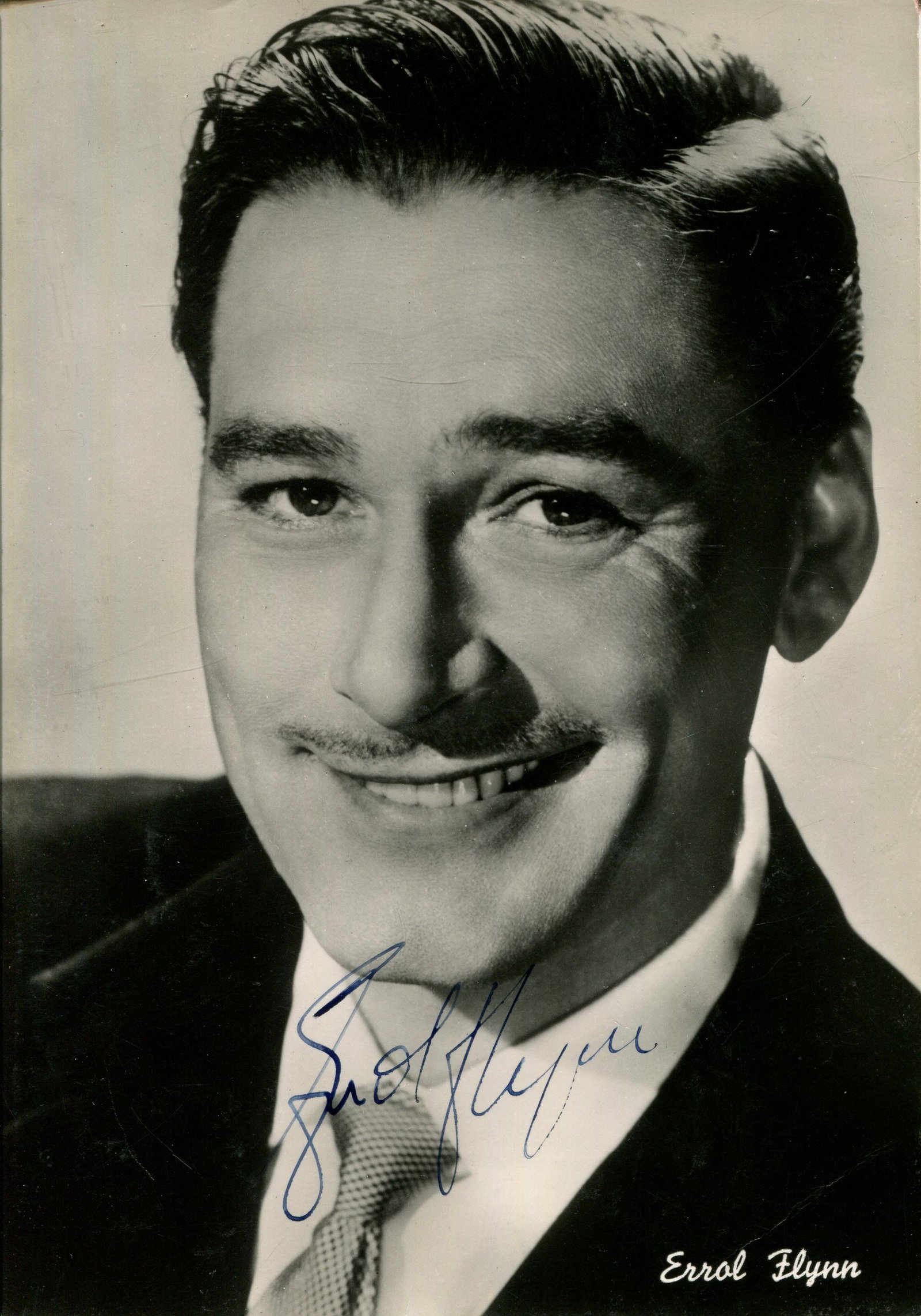 FLYNN ERROL: (1909-1959): FLYNN ERROL: (1909-1959) Australian actor. Vintage signed 4 x 6 postcard photograph of the suave Flynn in a smiling head and shoulders pose. Signed in fountain pen ink with his name alone across a