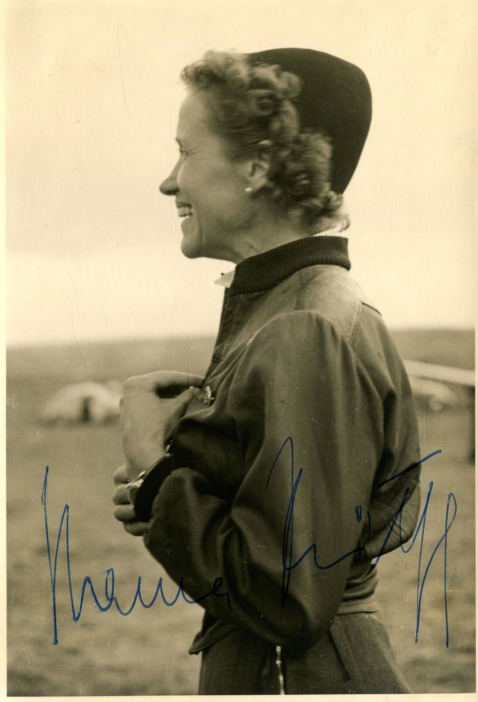 REITSCH & RIEFENSTAHL: REITSCH HANNA: (1912-1979) German aviatrix and test pilot who flight tested many of Germany's new aircraft during World War II. Signed 4 x 5.5 postcard photograph of Reitsch standing in a happy