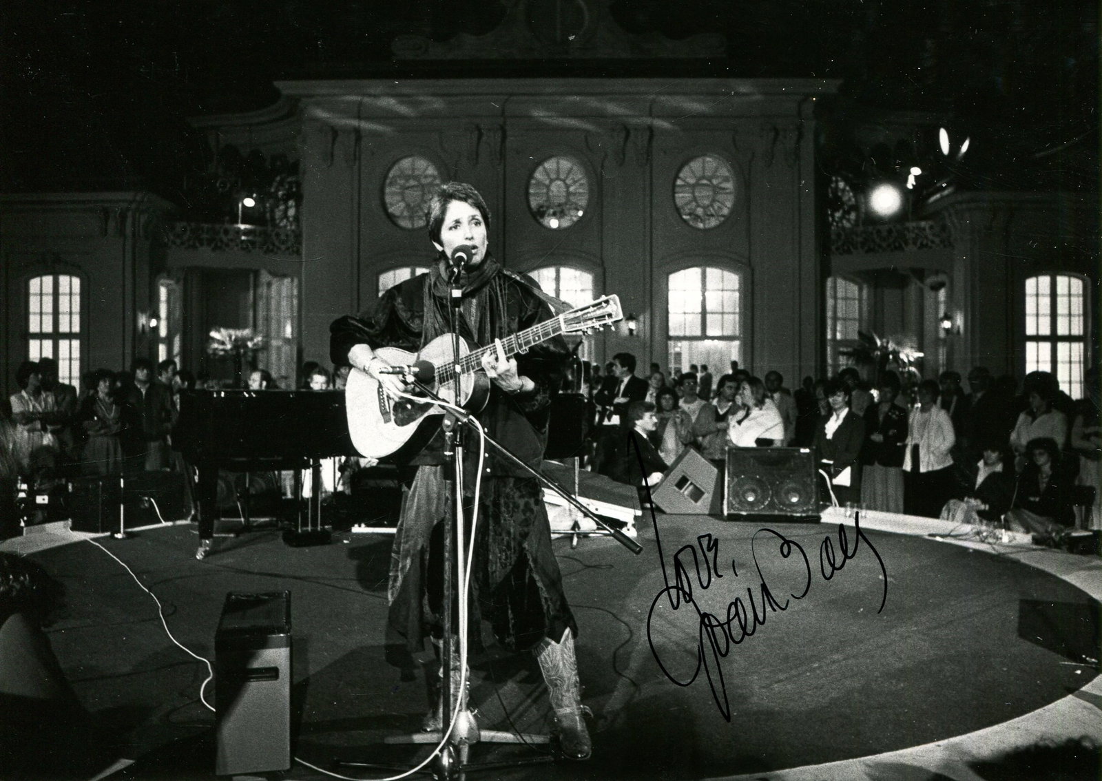 BAEZ JOAN: (1941- ): BAEZ JOAN: (1941- ) American singer. Unusual signed 5 x 7 photograph, the image depicting Baez seated in a full-length pose, singing and playing her guitar on scene, during a 1984 performance. Signed