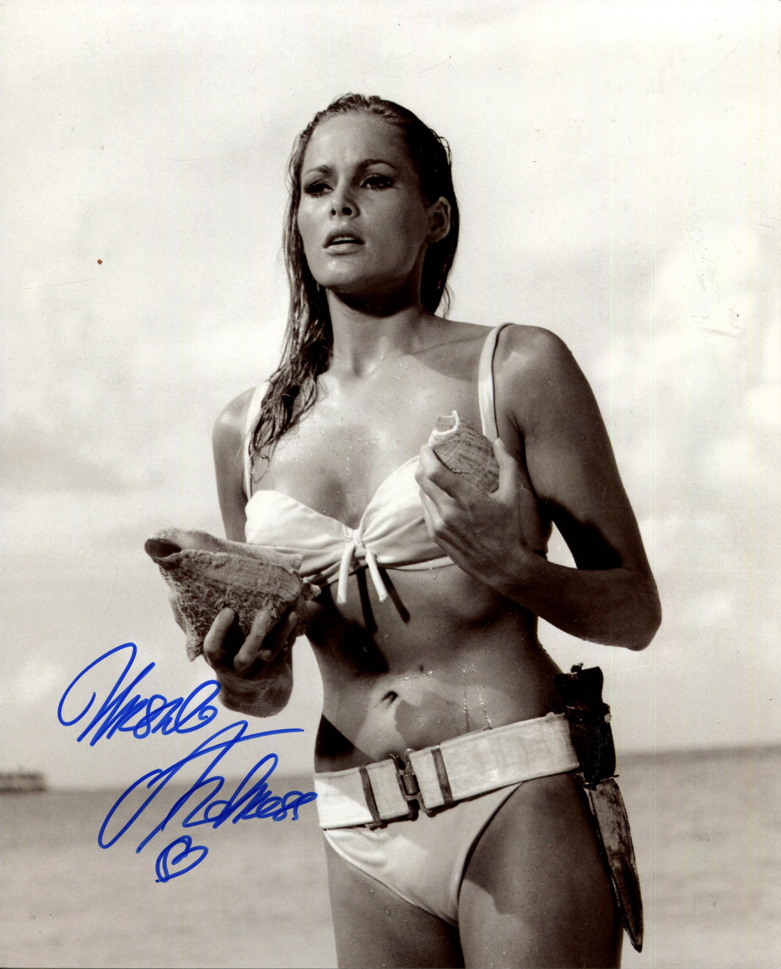 ANDRESS URSULA: (1936- ): ANDRESS URSULA: (1936- ) Swiss-German actress and sex symbol. Signed 8 x 10 photograph of the actress in an iconic half-length pose, holding a seashell and wearing a white bikini, in costume as Honey