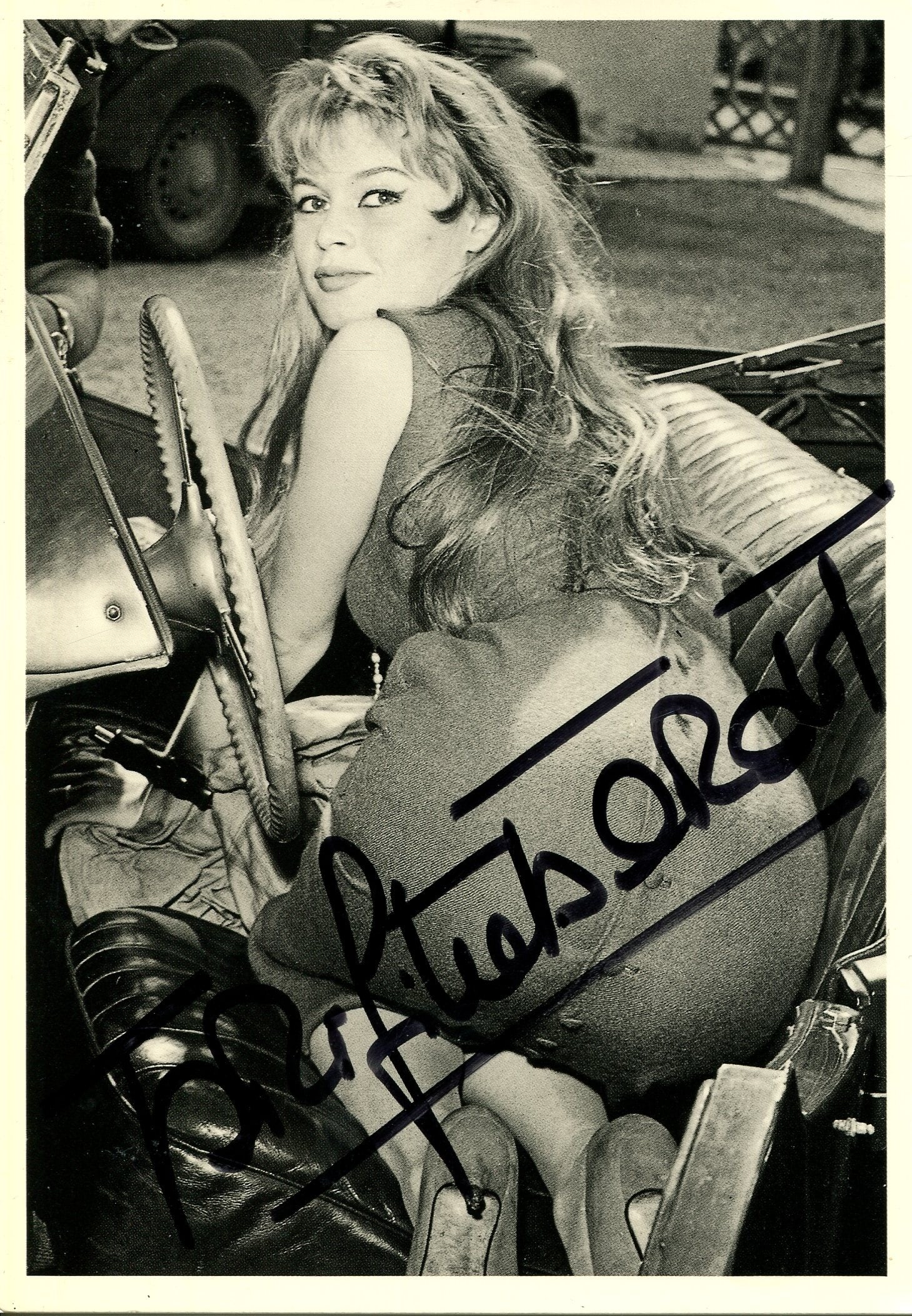 BARDOT BRIGITTE: (1934- ): BARDOT BRIGITTE: (1934- ) French actress and sex symbol. Signed postcard photograph, the image showing Bardot kneeling inside a convertible classic car, in a back full-length pose, with her face