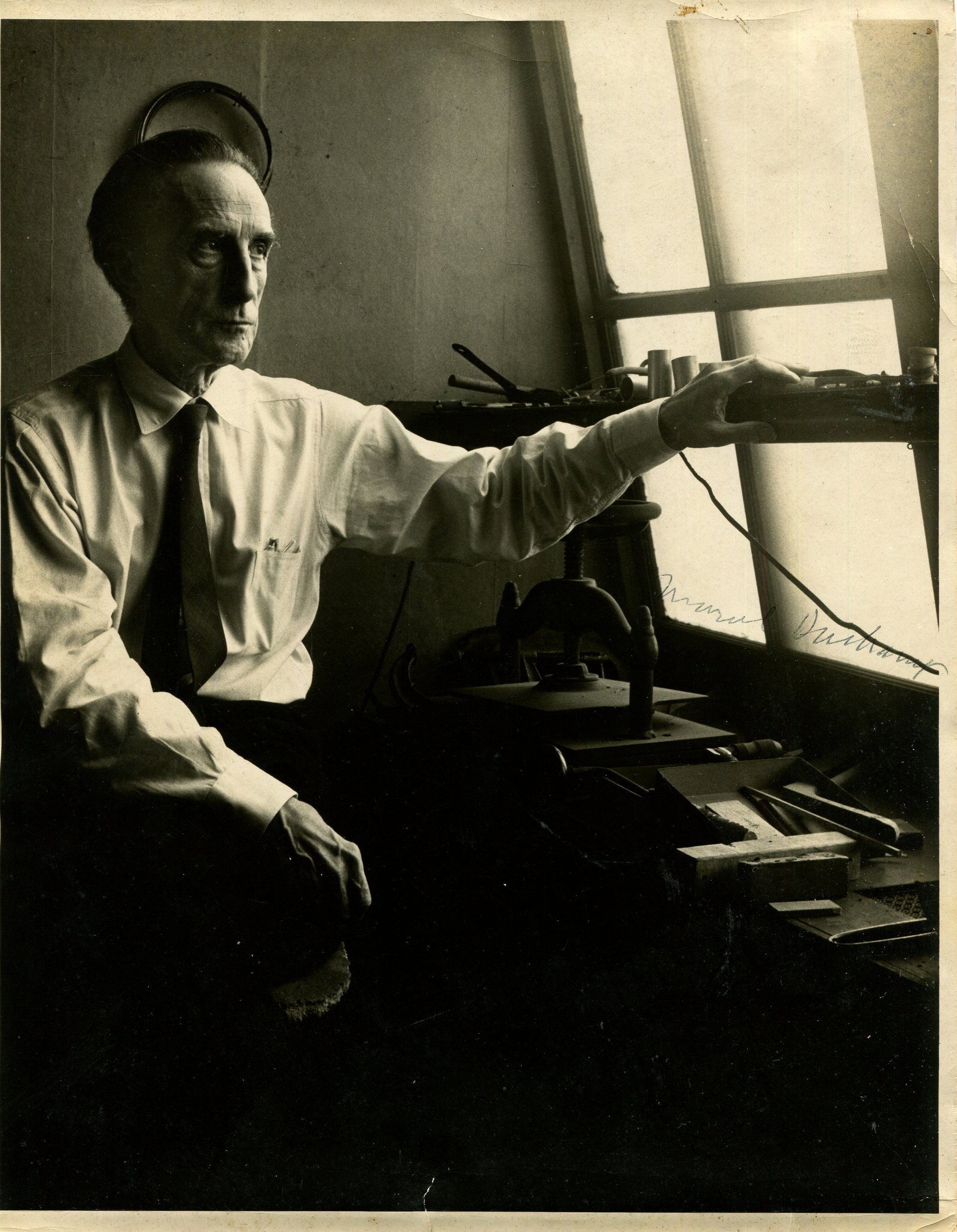 DUCHAMP MARCEL: (1887-1968): DUCHAMP MARCEL: (1887-1968) French painter and sculptor. An excellent vintage signed 8 x 10 photograph, the interestingly lit image depicting Duchamp, wearing a light shirt and dark tie, seated in a