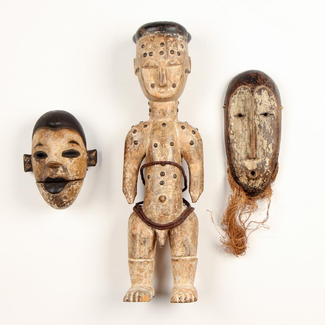 African Painted Figure and Two Masks: African Painted Figure and Two Painted Masks. Comprising two Lega masks, one with articulated jaw and metal teeth, the other with plant fiber beard; and one Atti standing figure with decorative metal 