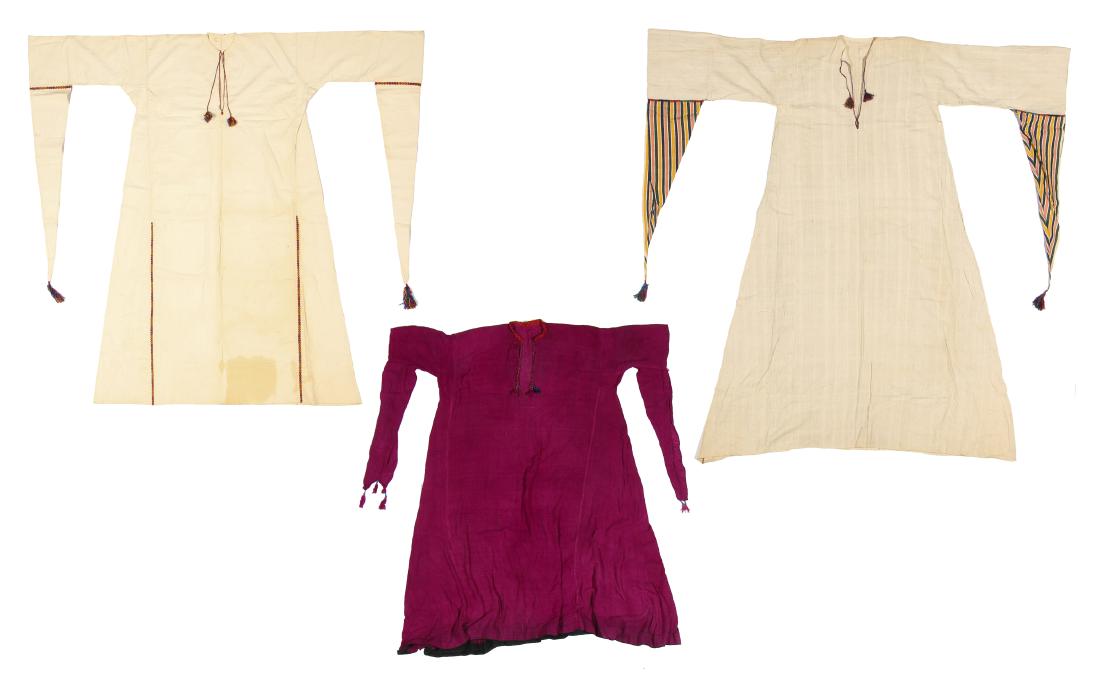 3 Antique Bedouin Thobes: Three antique thobes/caftan/dresses, probably middle eastern/bedouin with long triangular false sleeves, one with striped silk sleeve, one purple silk and two white cotton/linen. Beautiful silk embroi