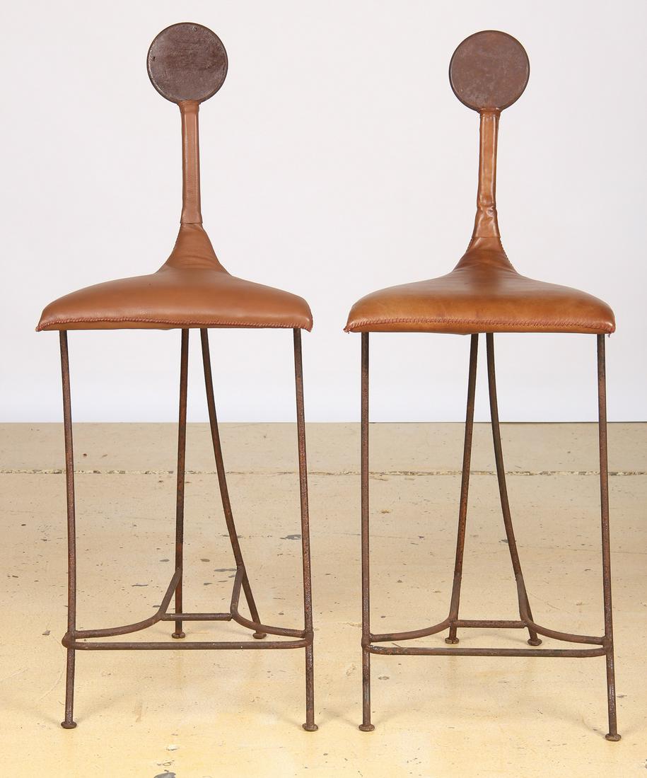 Pair of Artisan Iron frame barstools: Pair of Artisan Iron frame barstools, stitched brown leather covering, and decorative Cubist-style face on back. Each Size: 44.5'' x 14'' x 18'' (113 x 36 x 46 cm).