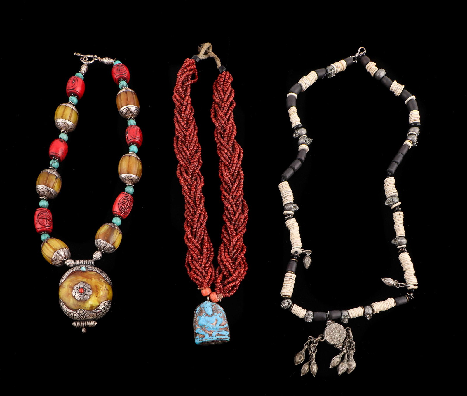 3 Tibetan and Nepalese Style Handcrafted Necklaces: Three Tibetan and Nepalese Style Handcrafted Necklaces. Including: 1) 12 plated red bead strands with blue figural pendant; 2) stone or shell disk necklaces with metal skulls and black beads, clasp ma