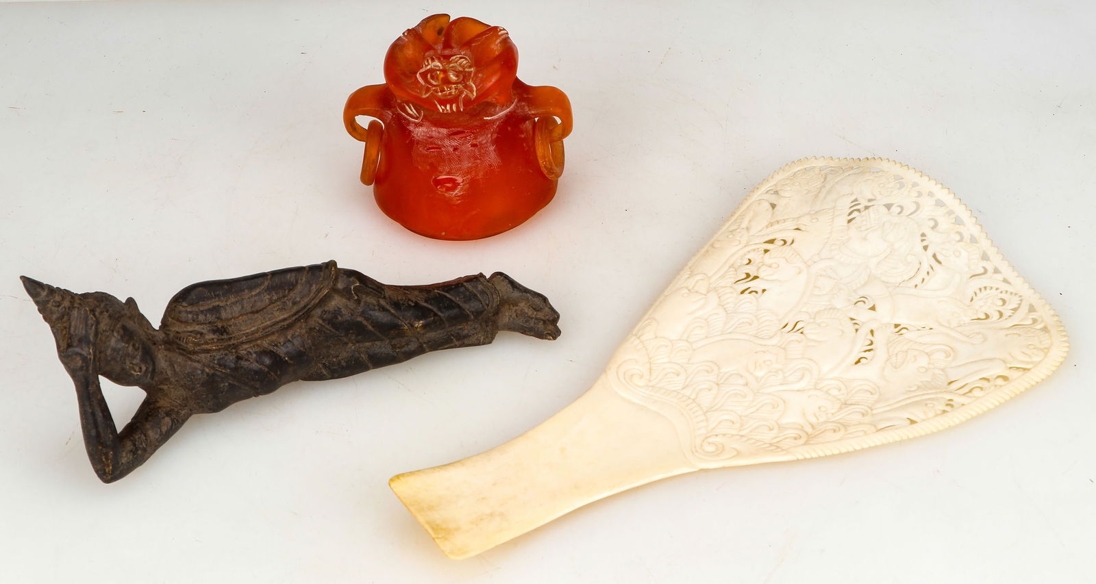 Ethnographic Collector's Lot: Ethnographic Collector's Lot. Including a Thai bronze reclining figure of Buddha, Length: 8" (20 cm) an Indonesian carved bone hand fan, Size: 11'' x 6'' (28 x 16 cm); and a Chinese carved amber lid.