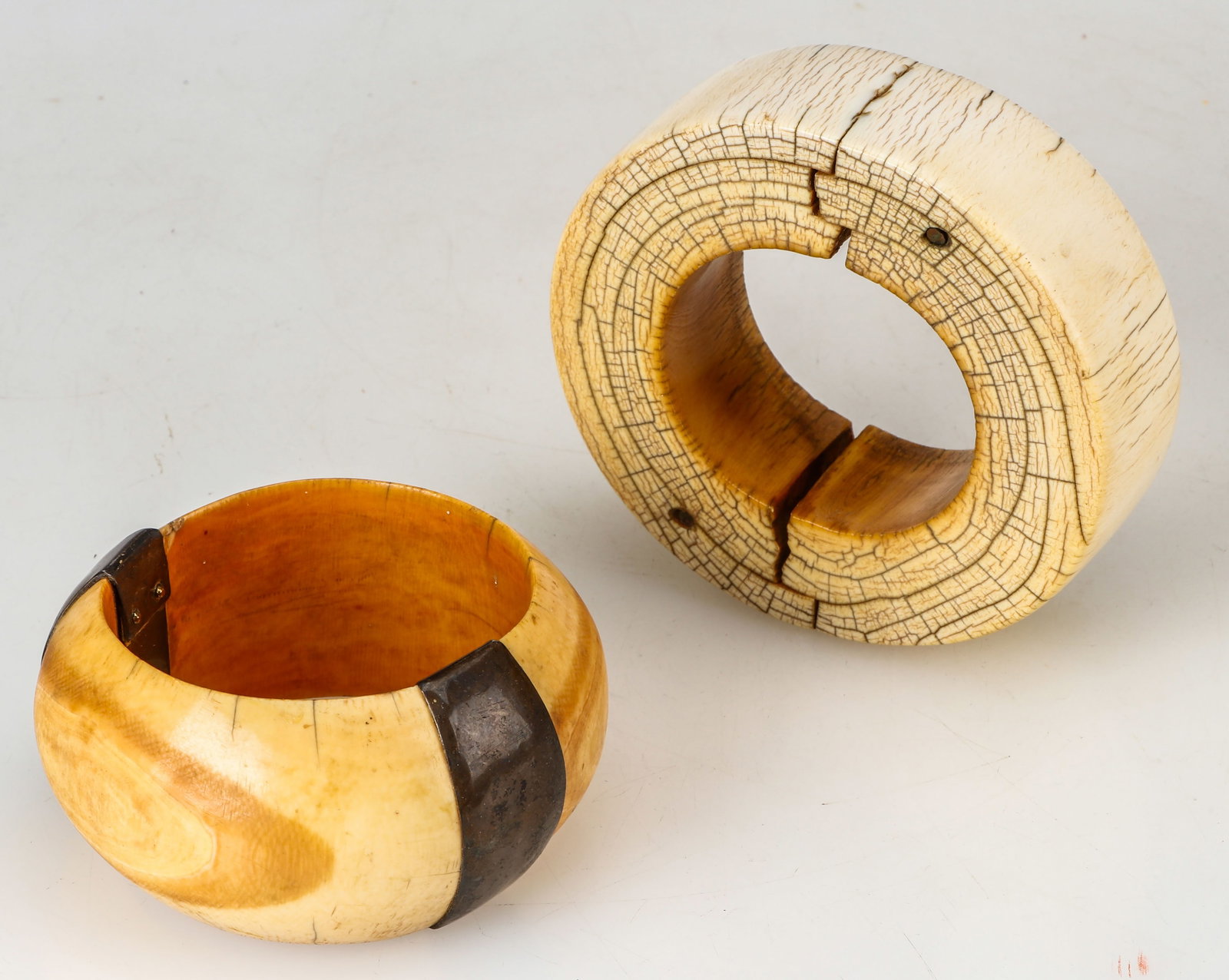 2 Antique African Bone Bracelets.: 2 Antique African Bone Bracelets. One with metal adornment. Sizes: 1) 1.5'' x 5'' x 5'' (4 x 13 x 13 cm); 2) 2'' x 4'' x 4.5'' (5 x 10 x 11 cm).