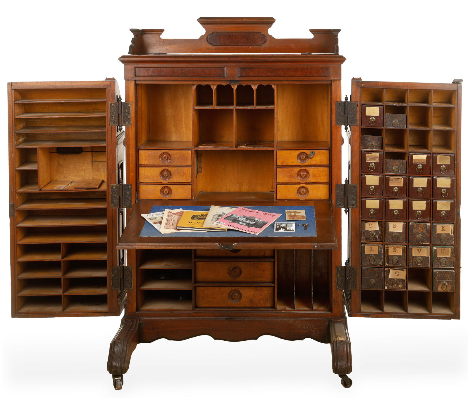 An American Walnut Wooton Desk: An American Walnut Wooton Desk. Of classic form with raised and molded panels, barrel top, and large hinged wings opening to reveal cubby holes, drawers and shelves, and flanking a drop front writing