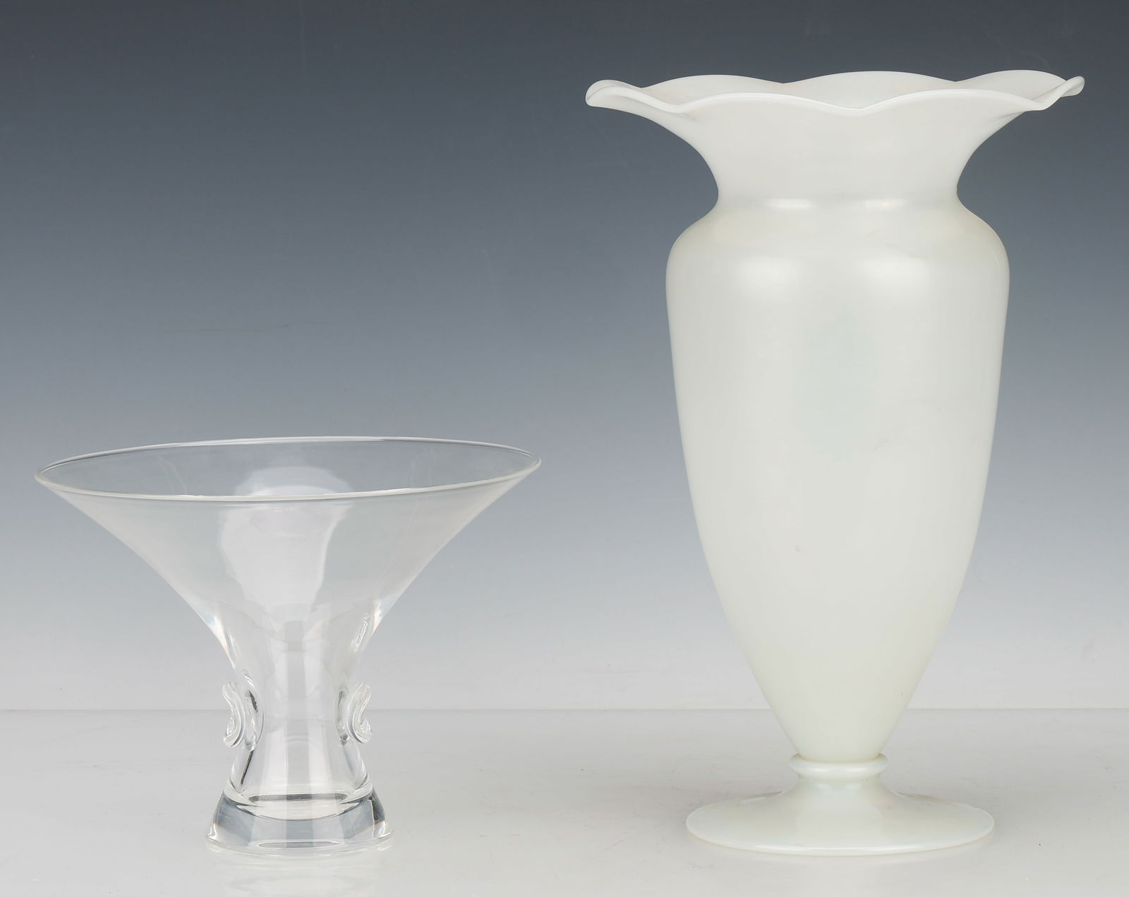 2 Steuben Vases: 2 Steuben Vases. One opaque white, the other clear, each signed. Sizes: 1) 5.25'' x 7'' x 7'' (13 x 18 x 18 cm); 2) 10.5'' x 6.75'' x 6.75'' (27 x 17 x 17 cm).