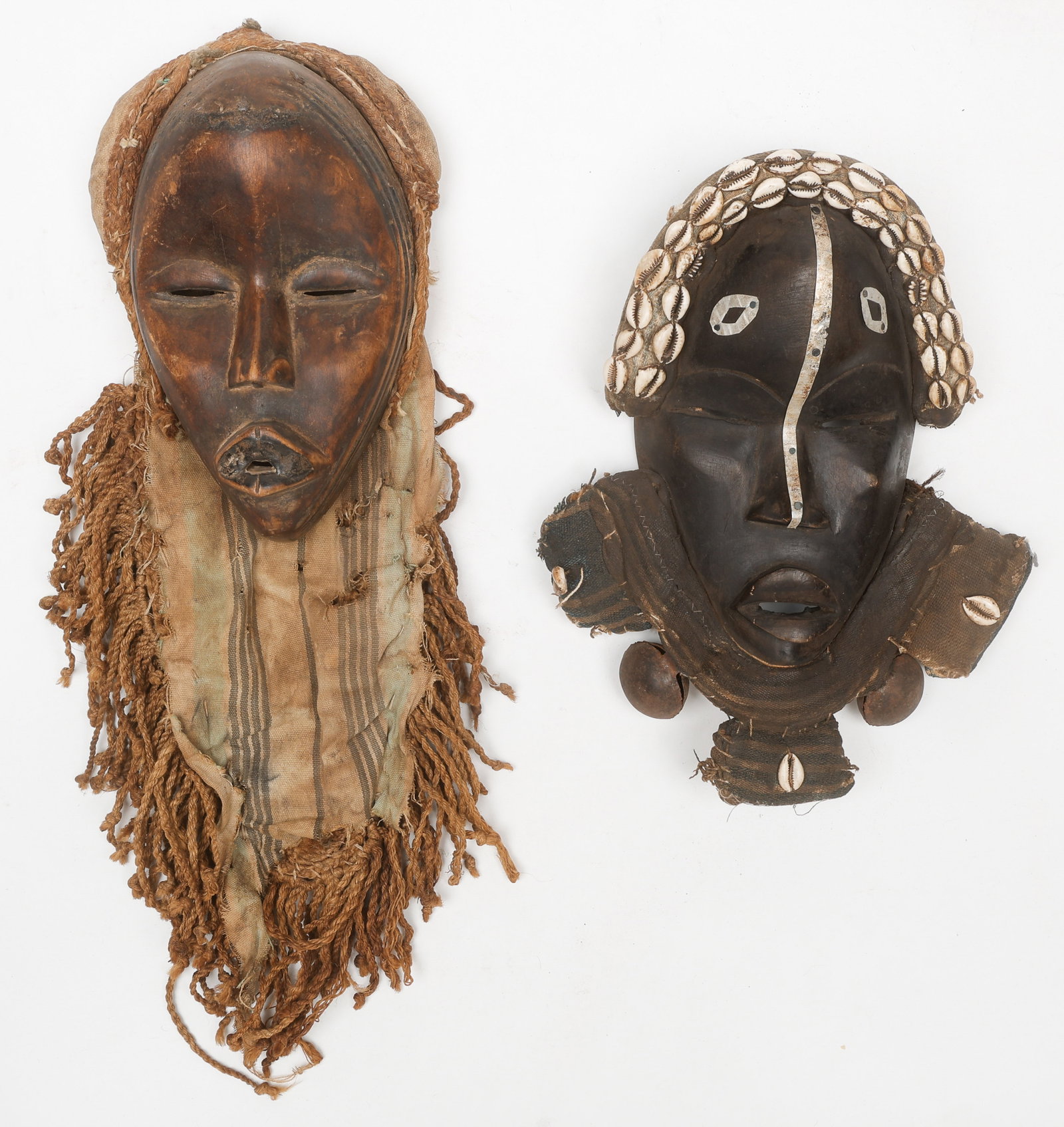2 African Dan Masks, Cote d'Ivoire: 2 African Dan Masks, Cote d'Ivoire. Carved wood, metal, plant fiber, and cowrie shells. Sizes: 1) 13.5'' x 11'' x 3'' (34 x 28 x 8 cm); 2) 21'' x 7'' x 3.5'' (53 x 18 x 9 cm). Provenance: Edna Coradin