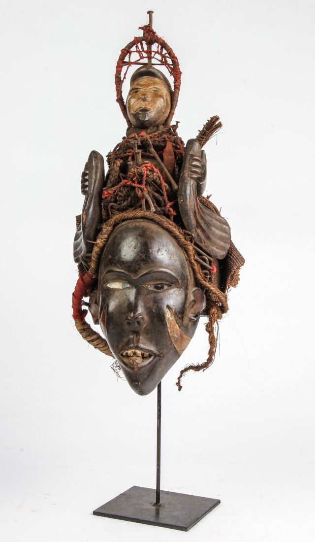 Kongo Mask Crested with a White Faced Nkisi: Kongo Mask Crested with a White Faced Nkisi. Carved wood with paint, fiber and nails. Size: 24" x 11" x 9".