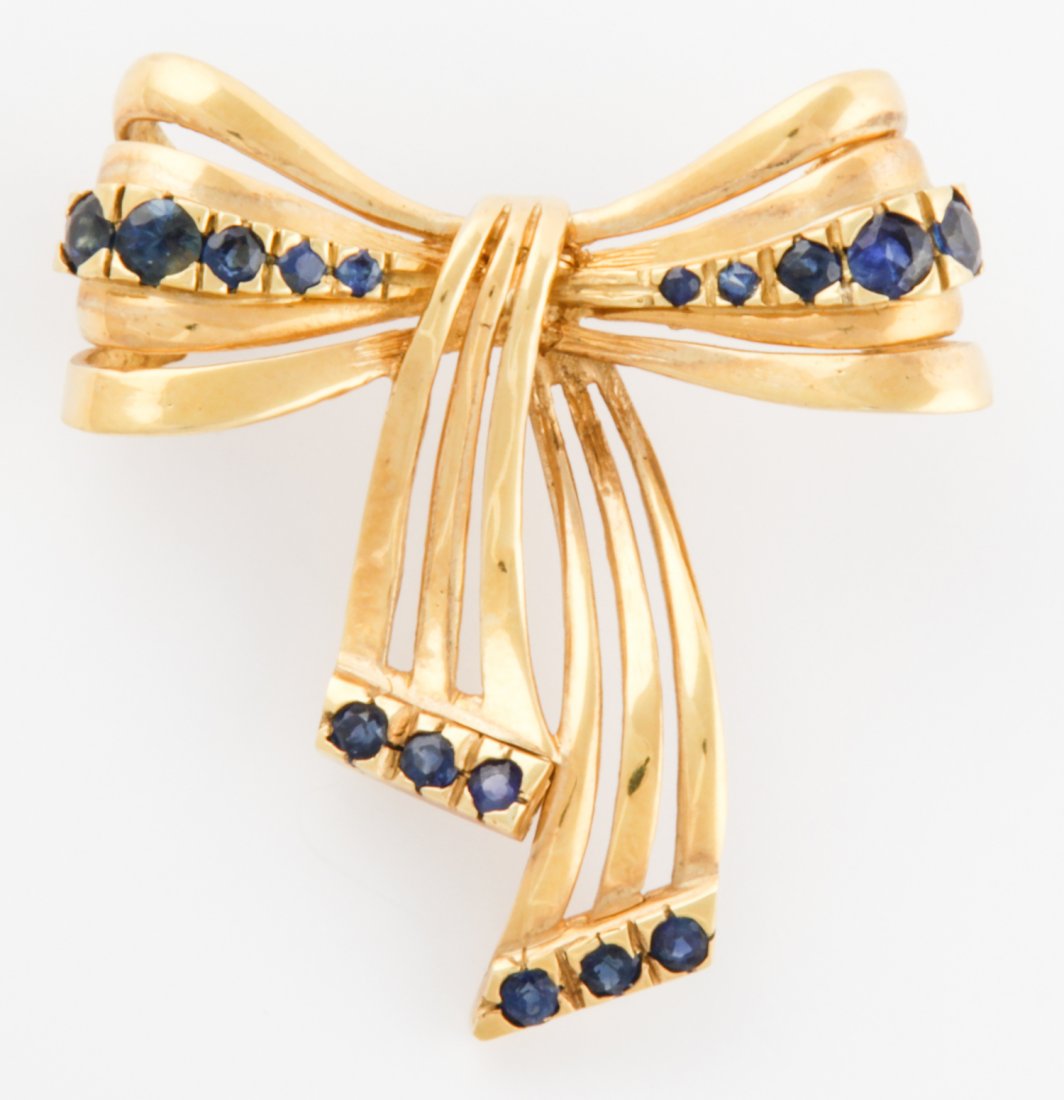 18K Gold and Sapphire Bow Pin: Gold and Sapphire Bow Pin marked 18K. Heavy. Size: 1.5" x 1.5" (4 x 4 cm). 10.6 g. Since 1937, the The Silver Shop of Princeton, NJ was located at 59 Palmer Square West.