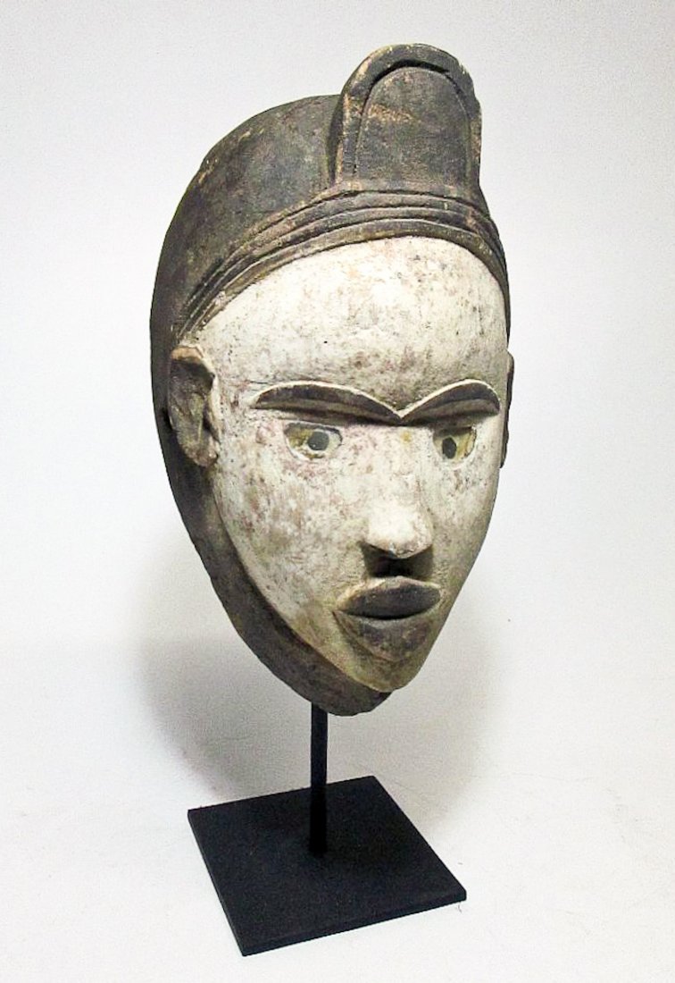 A Kongo African Mask: A Kongo African Mask. Carved wooden mask with kaolin clay pigment and inset glass eyes. The wood of this mask is very light weight with age. Size: 14" x 7.5" (36 x 19 cm). Includes base.