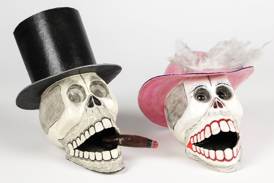 2 Antonio Joel Garcia (Mexican, b. 1955) Skulls: 2 Antonio Joel Garcia (Mexican, b. 1955) Skulls (Calaveras): a Male skull in a black top hat with lit cigar between his teeth and a Female skull wearing pink hat with white feathers, each free standin