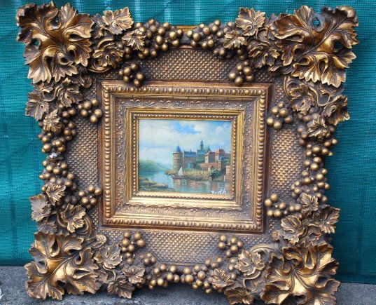 Magnificent Oil on Canvas Painting of European Castle: Magnificent oil on canvas painting depicting a European castle with sail boat in river. Signed. Framed in a beautifully detailed, heavy gilded frame with grapes and leaves. Measures approx. 30 inches