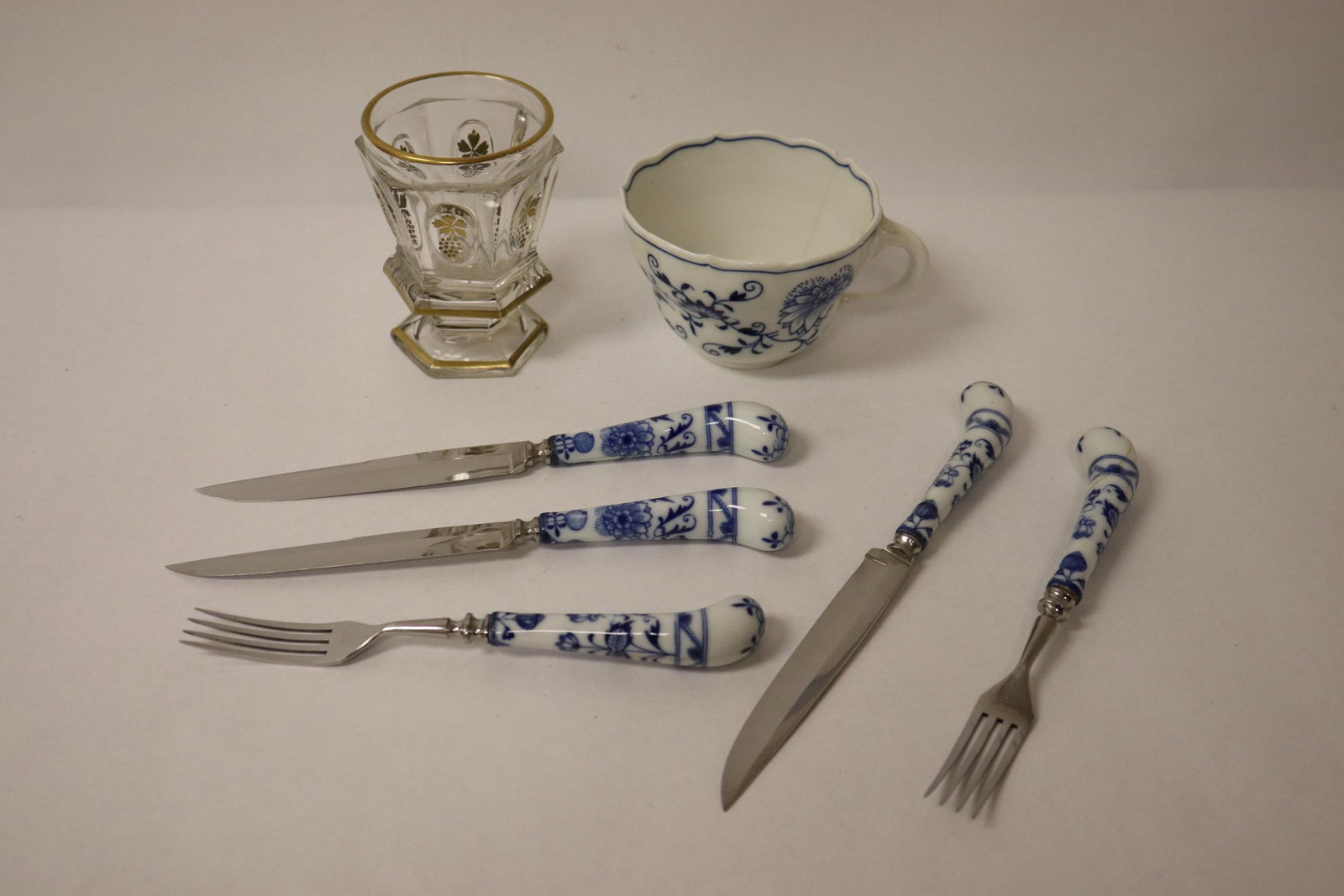 7 pieces: A Meissen cup (chip, 2.75"Hx4.8"x3.85"), 5 Meissen(?) knives/ folks (chips/ crack, 7.25"L(2), 8.5"L(3)), and a Belleek cup (3.95"Hx3.05"dia)