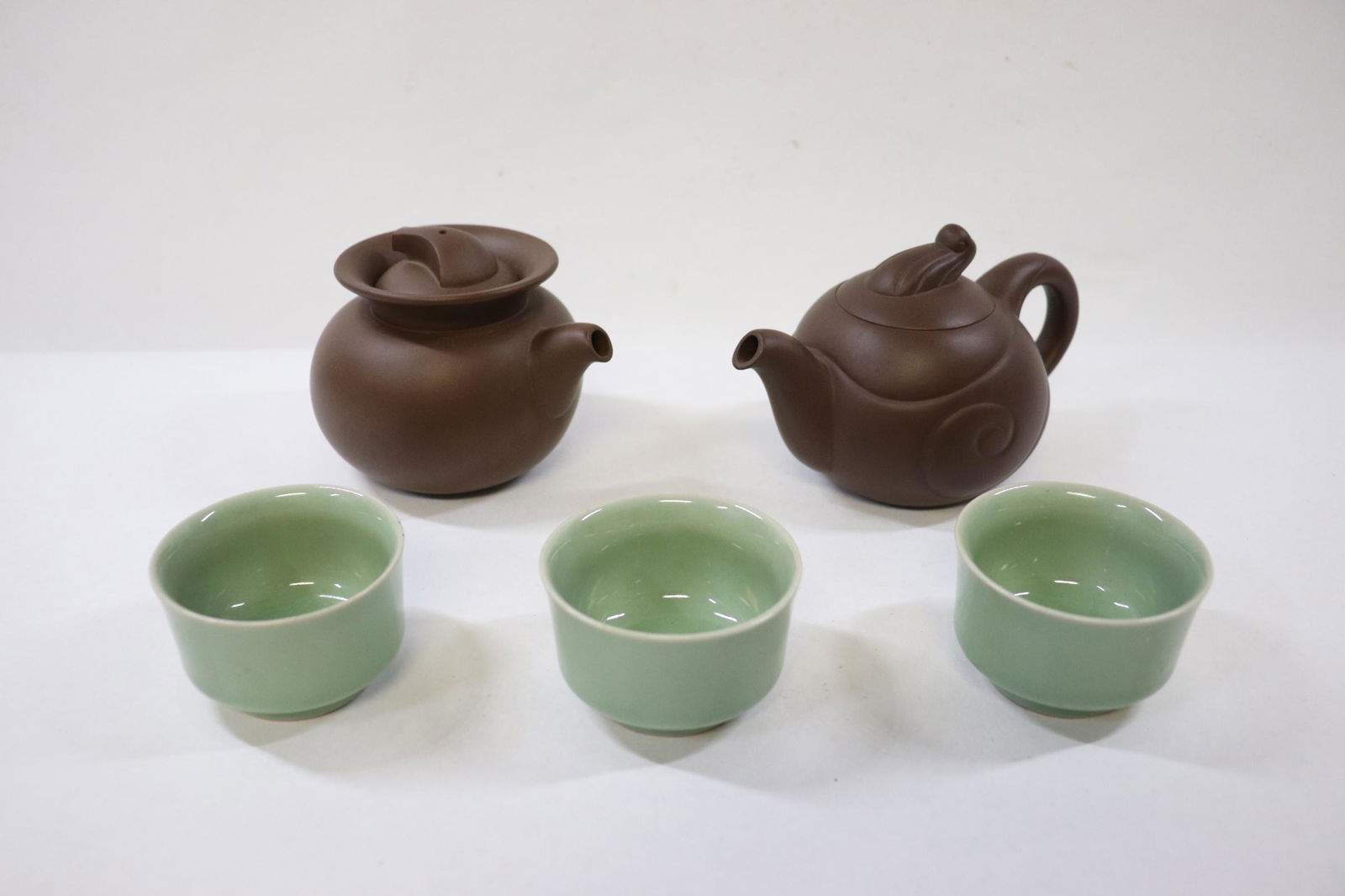 2 Yixing teapots and 3 celadon tea cups: 2 Yixing teapots (3.45"Hx4.25"x3.5", 3.45"x5.7"x3.4") and 3 celadon tea cups (1.6"Hx2.65"dia(3))