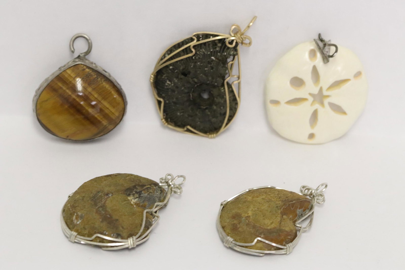 lot of misc.: 2 silver framed fossil pendant, one GF framed fossil pendant, a silver pendant with tiger eye stone, and a bone carved pendant