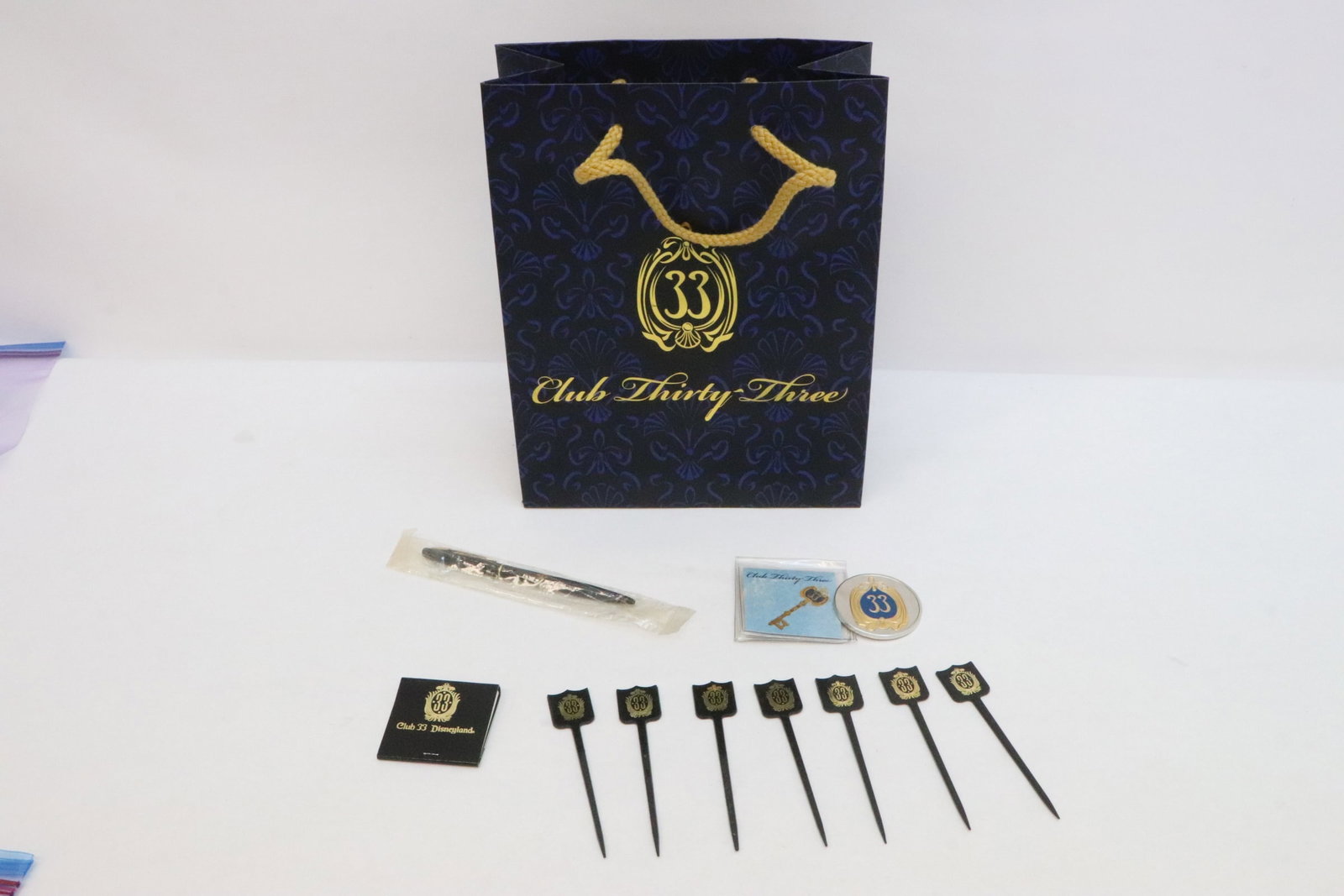 Lot of club 33 items: Lot of club 33 items; a 2017 silver tone challenge coin (0.16"x1.84"dia) features club 33 logo and Mickey holding a club 33 key, a club pen (5.16"L) in original seal, a Mini notepad pack, 6 club 33 sw