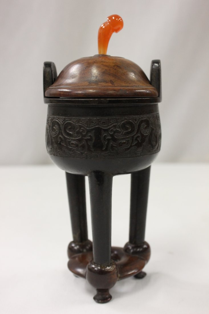 Chinese antique bronze ding: Chinese antique bronze ding, it stands on 3 long legs, the 2 handles rose on side, the body decorated with taotai pattern in relief. Wood carved cover with carnelian finale, fitted rosewood stand (pos