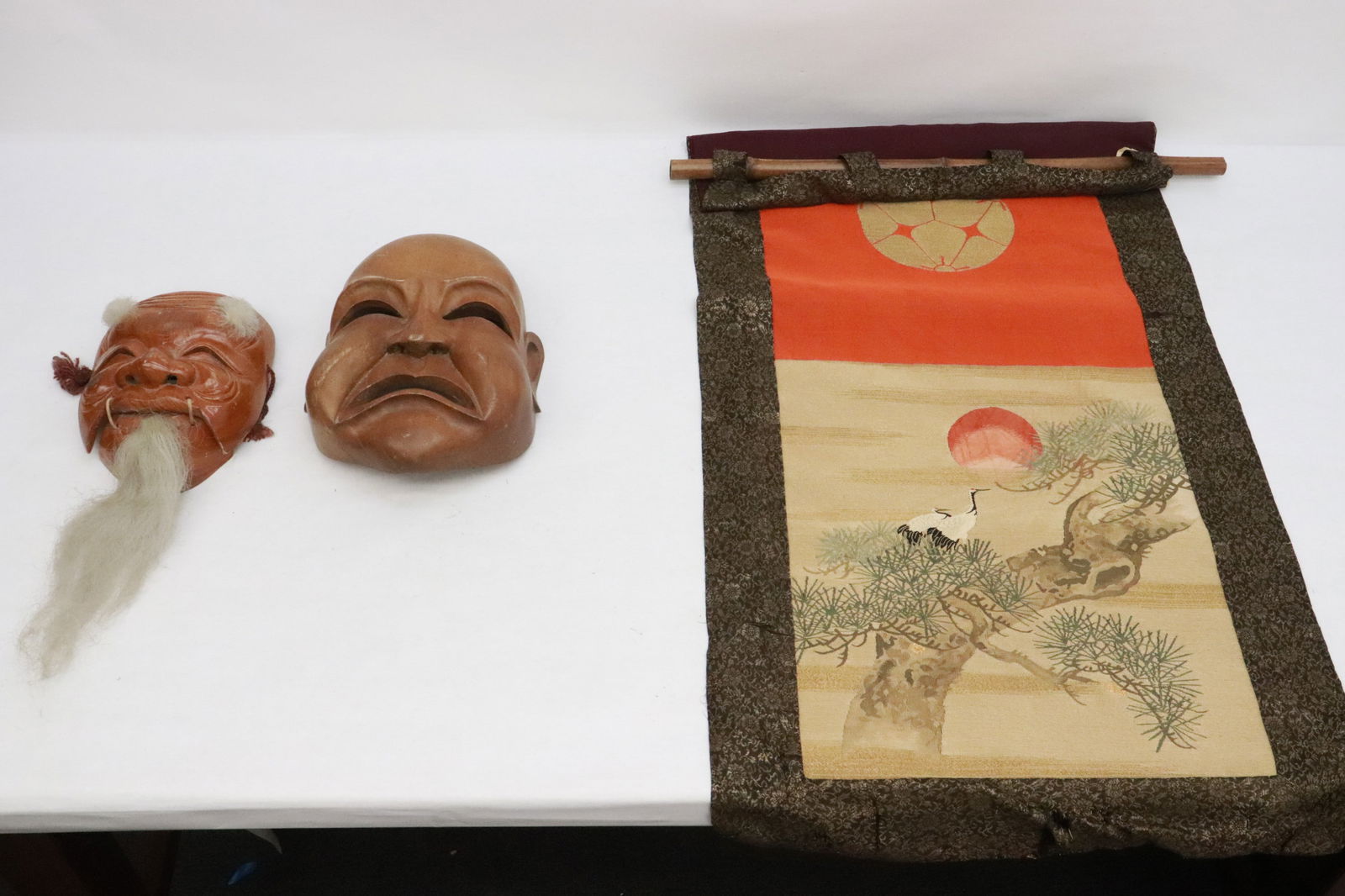 2 wood carved masks, & an embroidery style panel: 2 Japanese wood carved masks (8"x6.5"x2.9", 10.2"x7.65"x3.8"), and a Japanese embroidery style panel (38"x18.6")