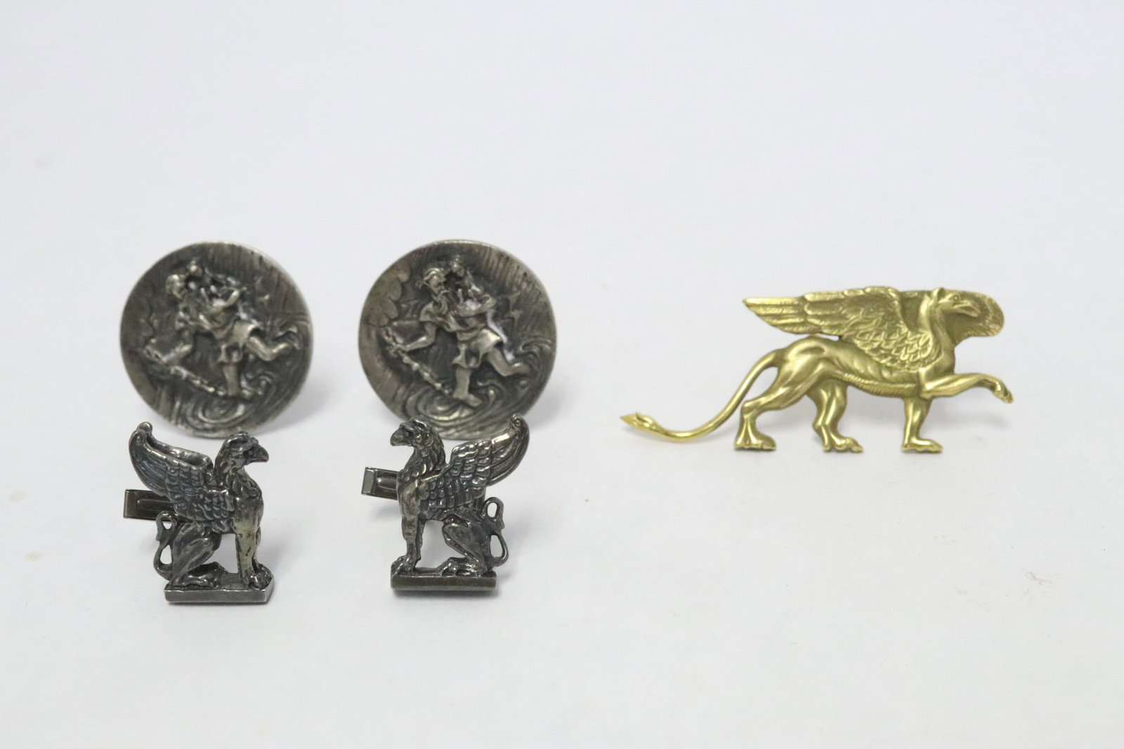 2 pairs of sterling cufflinks, & a yellow metal brooch: 2 pairs of sterling cufflinks (one with religious scene in relief (1.2"dia ea), one in the form of griffin (0.9"x0.68" ea), total wt. 46gm), and a yellow metal brooch (1"x2.3") in the form of griffin