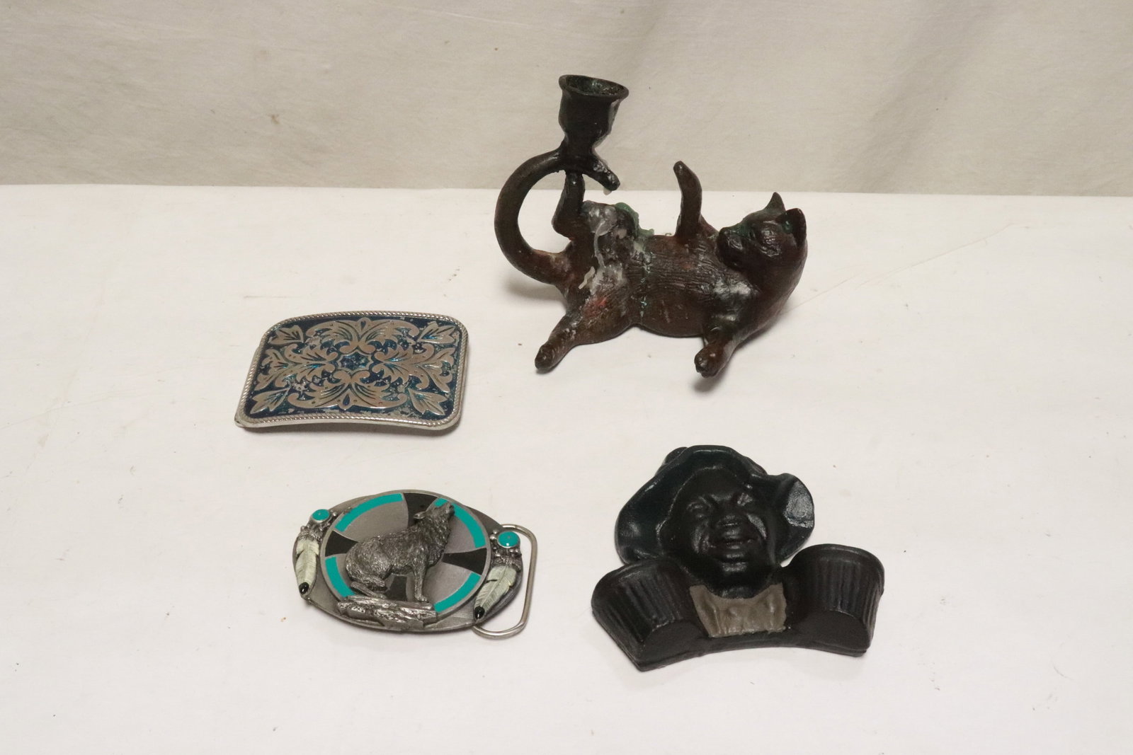 4 pieces: 4 pieces; a bronze candle holders (4.25"x5.1"x3.45") in cat motif, a cast iron wall hanging ornament (3.9"x4"x1"), and 2 belt buckles (2.4"x3.45", 2.63"x3.65")