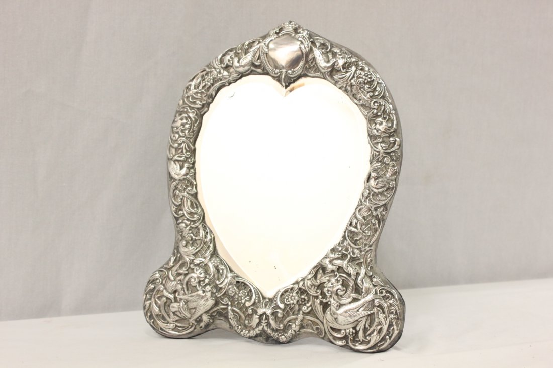 A sterling framed table mirror with beveled glass: A beautiful sterling framed table mirror with beveled glass, the sterling border decorated with birds and flowers in repose fashion, 12.7"x10.25"