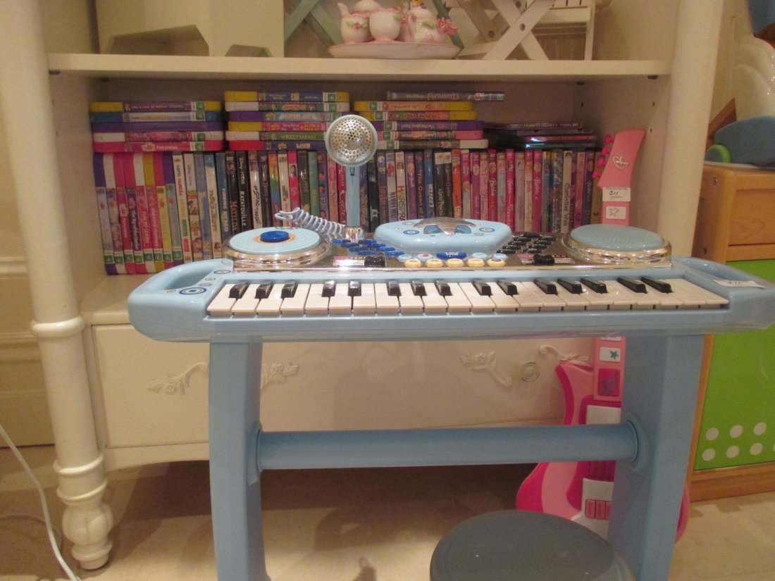 A shelf of childrens DVDs, a toy piano and a guitar:  A shelf of childrens DVDs, a toy piano and a guitar