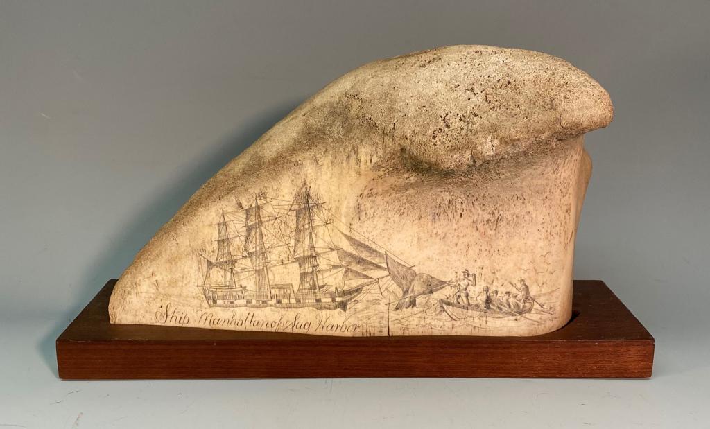LARGE 19" SECTION OF SCRIMSHAWED WHALE BONE: WITH DETAILED SCRIM OF THE BOAT 'THE MANHATTAN' OF SAG HARBOR, PLACED INTO A CARVED BOARD FOR DISPLAY; BONE ITSELF MEASURES 19" ACROSS AND 9" HIGH