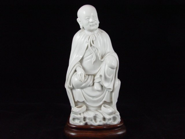 074: Fine 17th Century Chinese Blanc De Chine Statue: Sitting in long robes, both hands resting on knees, his shoes lift on the lower section of the rockwork set, included wood stand, from the 17th Century. He is 4.5 inches wide and 10.5 inch tall with t