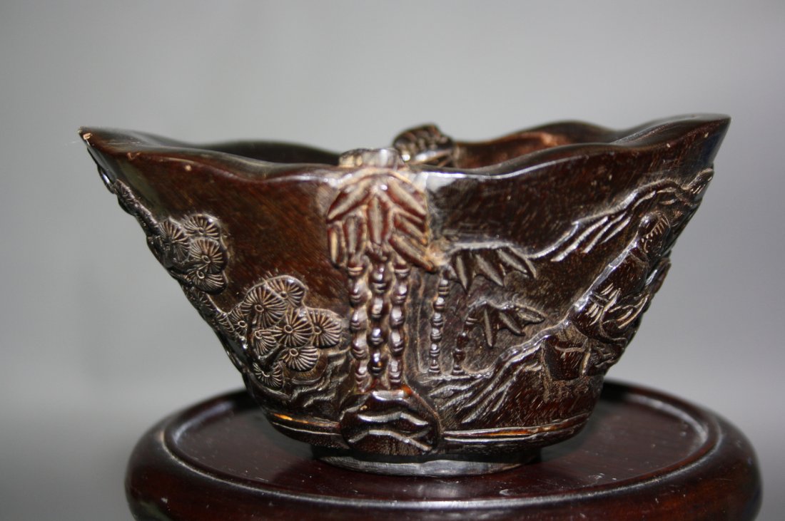 Rhinoceros Libation Cup: Rhino horn carved in the shape of Yuan Bao, fine detailed carving of a motif of lotus, figures, bats and leaves. Sizes: 6cm x 12cm.