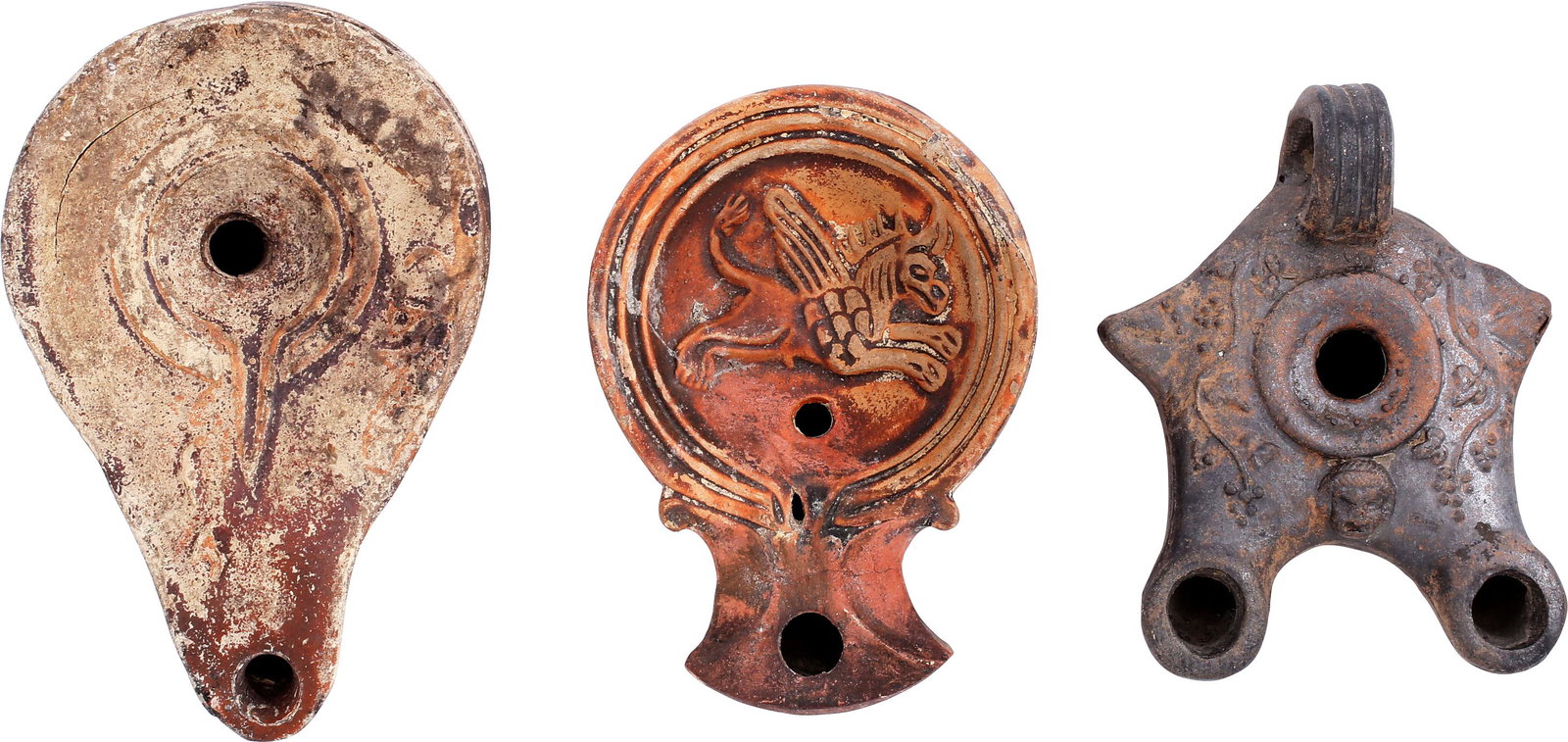 GREEK/ROMAN OIL LAMPS: Lot of three, undated. Largest, 3 7/8” plain form with remnants of red decoration. Second with flared spout and unicorn motif. Third with two spouts and cherub face.