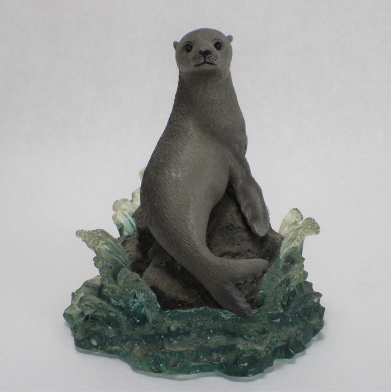 Wyland "Baby Harp Seal" No. 4029: Measures approximately 4.5 inches tall x 3 1/4 inches wide. This sculpture depicts a Harp Seal pup sitting on a rock, looking over its shoulder. The blue, translucent waves crash upon hitting the rock