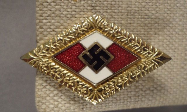 German WWII Golden Hitler Youth HJ Honor Badge: German World War II Golden Hitler Youth HJ Honor Badge With Oak Leaf Rim. Has a thin pin back. Maker marked 'RZM BM 1/122'. Two piece brass and enamel construction