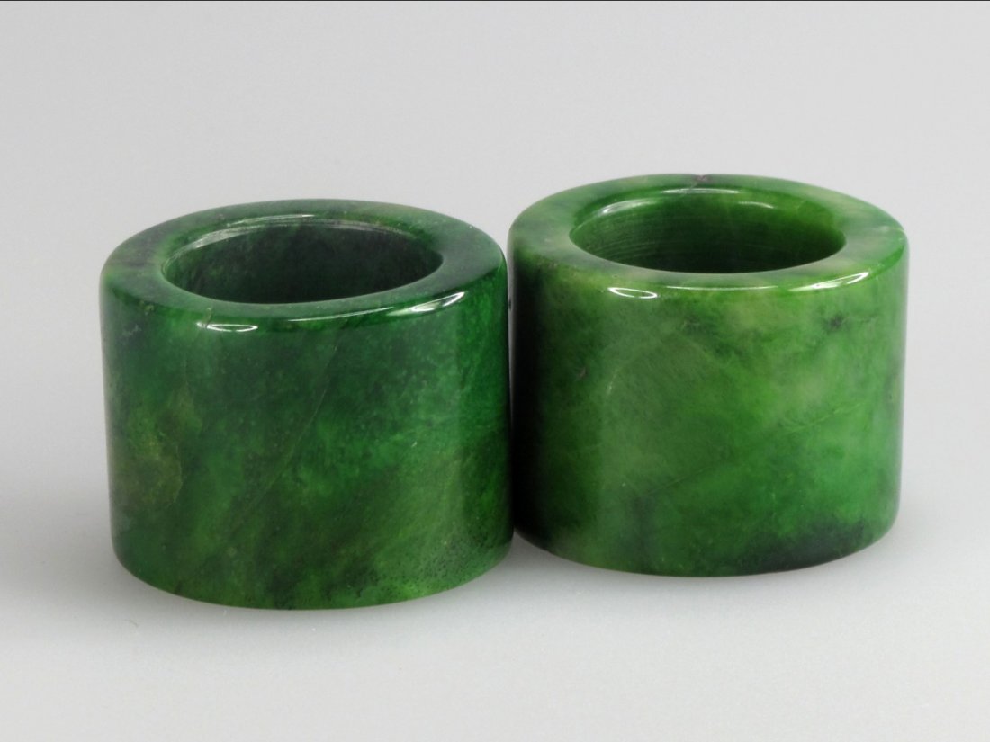 Two Chinese Spinach-Green Jade Thumb Rings: Chinese green jade items, a pair of semi-translucent emerald colored thumb rings suffused with dark splashes. D: 3.5 cm