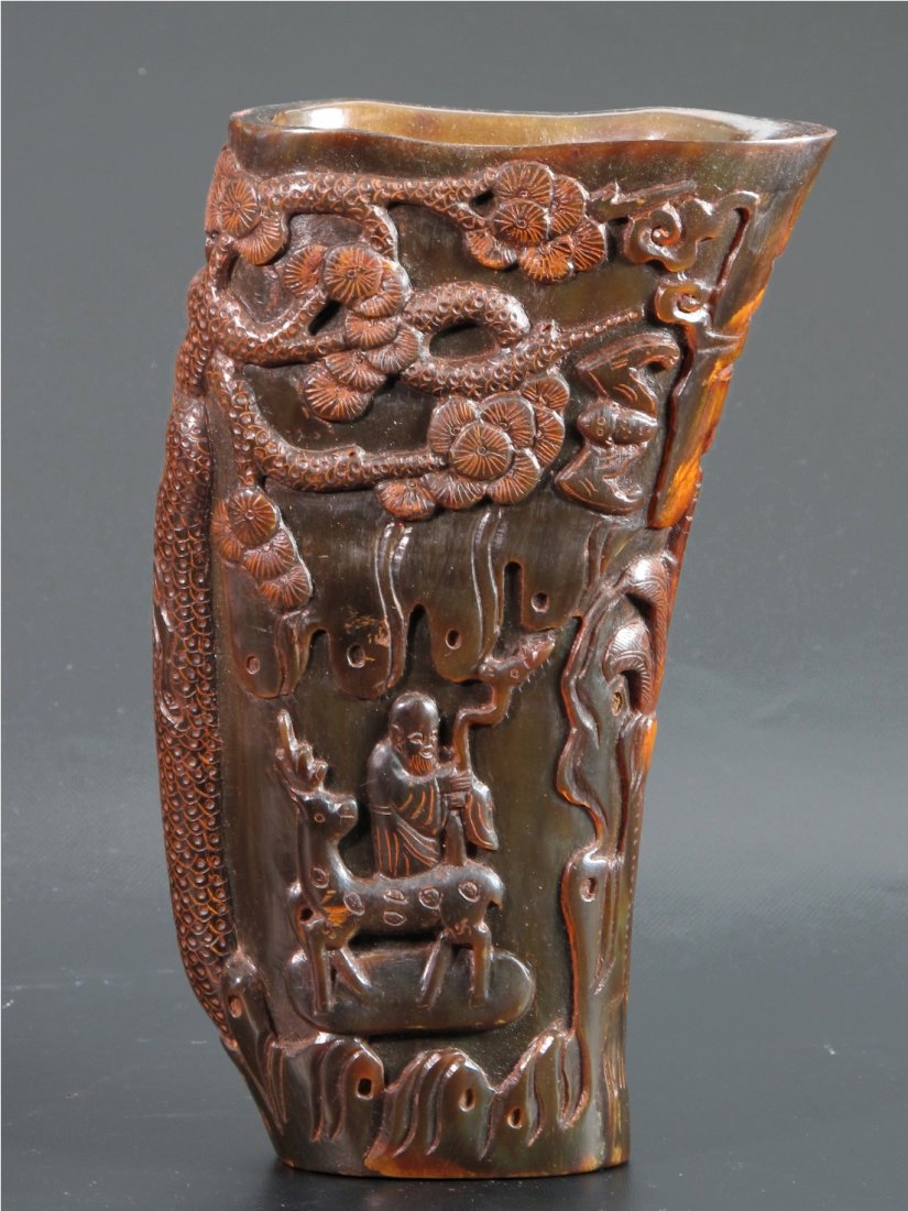 A Chinese Carved Horn Libation Cup: In natural curved form and carved with the immortal and their acolytes under the large pine tree. H: 16.5 cm