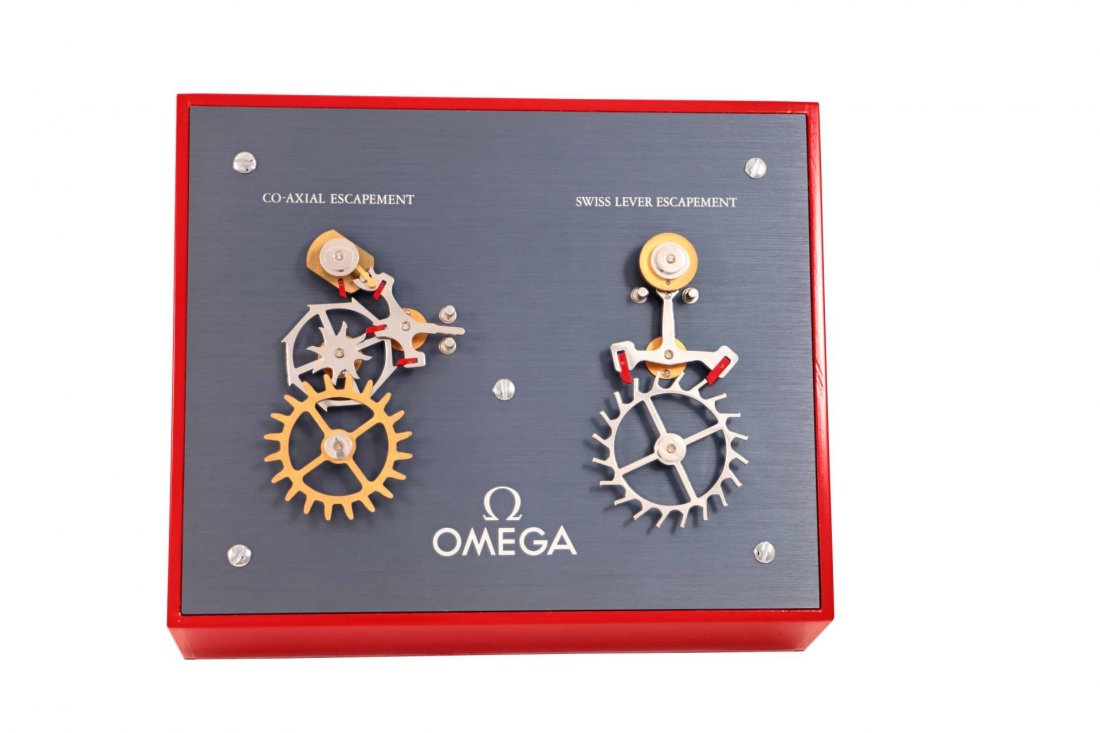 Omega Moving Display Speedmaster Escapement Machine: Brand: Omega Model: Electrical Demonstration Display Co-Axial Escapement VS Swiss Lever Escapement Dimensions (Approximate): 30cm x 25cm x 12cm Material: Wood/Metal Movement: 220