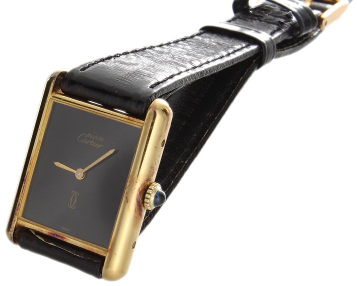 Must de Cartier Tank Vermeil Swiss Mechanical Watch: Yellow gold filled Must de Cartier Vermeil wristwatch with a blue cabochon crown. Swiss made, mechanical movement. Black dial. It comes on a generic black eel skin band with a generic tang buckle. It