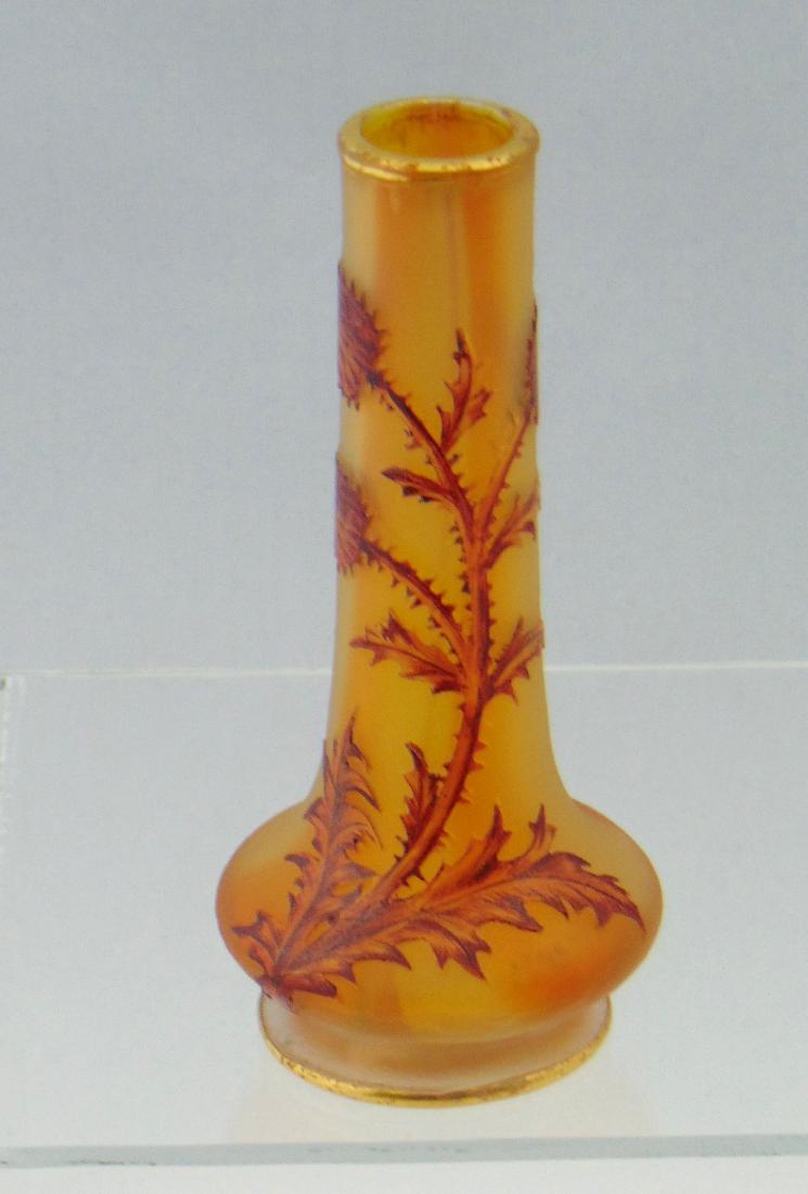 Daum Thistle stick glass vase: Footed stick vase in amber and rose decorated with a Crimson stemmed thistle, signed Daum Nancy, 4 1/2' ht. Condition: good but with slight gold loss on the rim