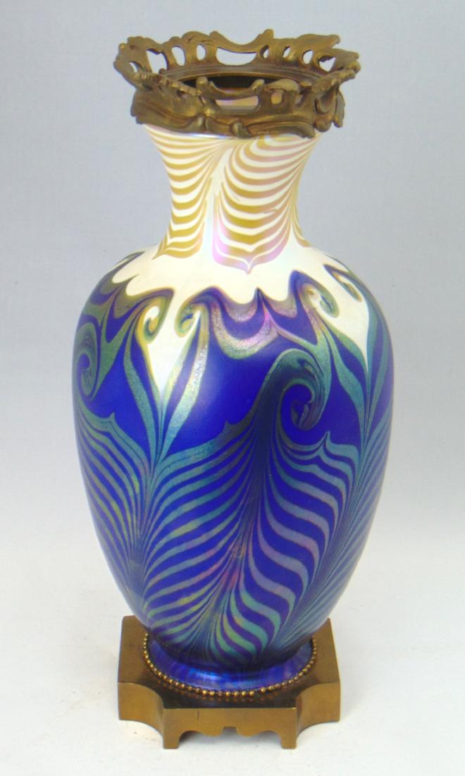 Quezal art glass lamp base: Shouldered form in blue to opal glass decorated with an iridescent gold hook feather design fitted with a metal foot and rim, Overall 14" ht. Condition: one closed bubble on body