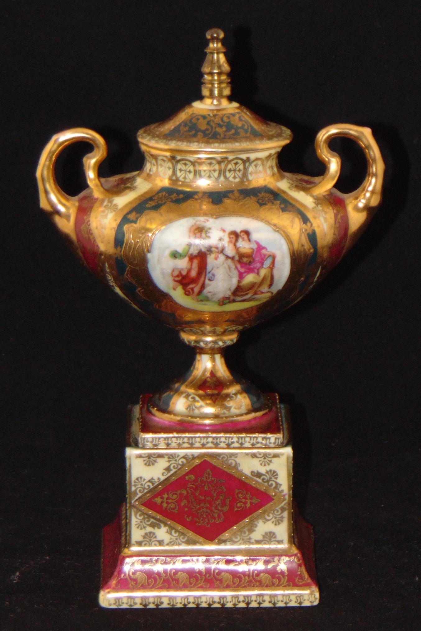 Royal Vienna porcelain covered jar,: Two handled covered urn in red and green with strong gold highlights decorated with a central hand painted medallion of laughing women, marled with a beehive back stamp, 9" ht. Condition: minor enamel