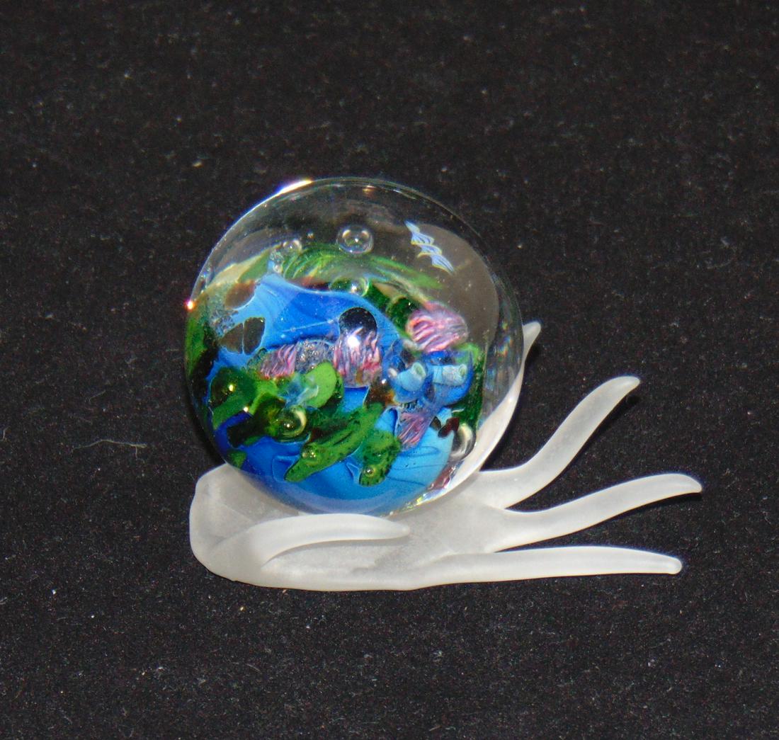 Josh Simpson paperweight: Blue orb paperweight with bubbles and helix signed JS 04, set on a glass figural hand, orb only 1 3/4" wide. Condition: good with no defects found.