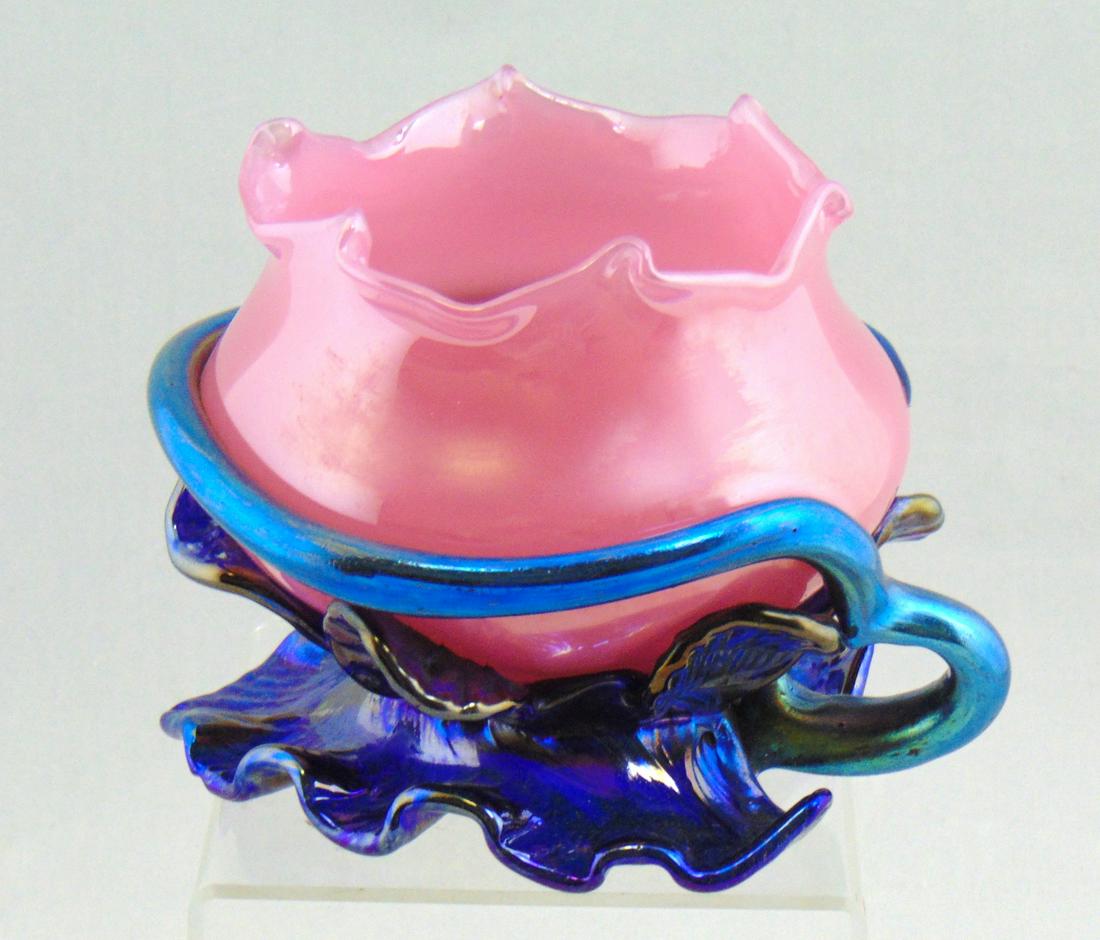 Loetz pink and blue rose bowl: Ovoid form in pink glass adorned with a iridescent blue leaf form foot and applied snake, marked with an acid stamp Czecho-Slovakia, 4" ht. Condition: good with no defects found.