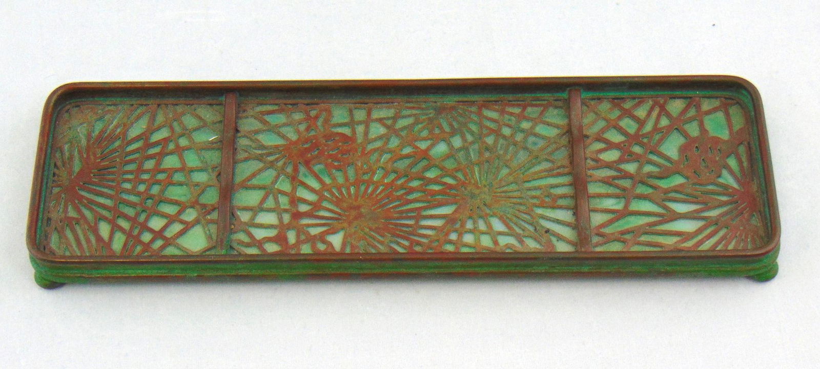 Tiffany glass and metal tray: Elongated pen tray in green glass framed with the pine needle design, marked Tiffany Studios New York 1004, 9 1/2" long. Condition: good with no defects found