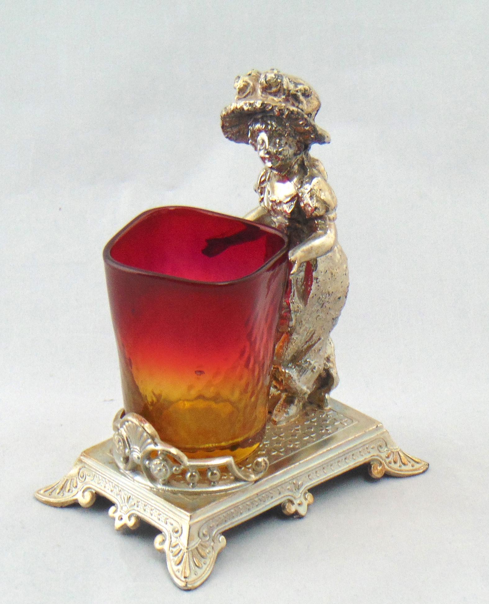 Kate Greenway Amberina toothpick: Cylindrical Amberina optic diamonds toothpick set in a figural Kate Greenway Tufts holder with a female child, 5" ht. PROVENANCE: Earlys Auction to the Black collection. Condition: glass good with no 
